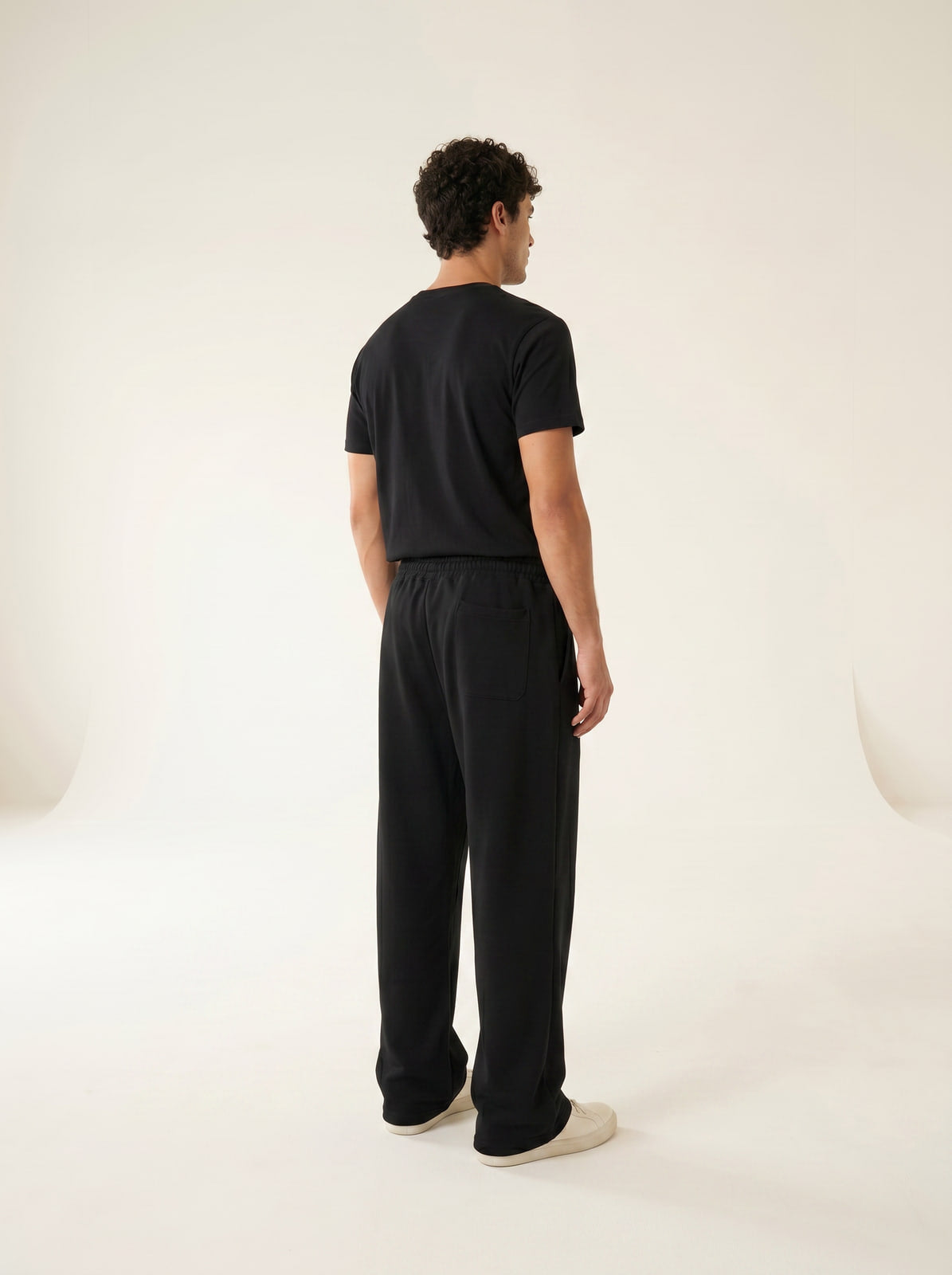 Black wide-leg sweatpants, back three-quarter view showing drape, cream studio